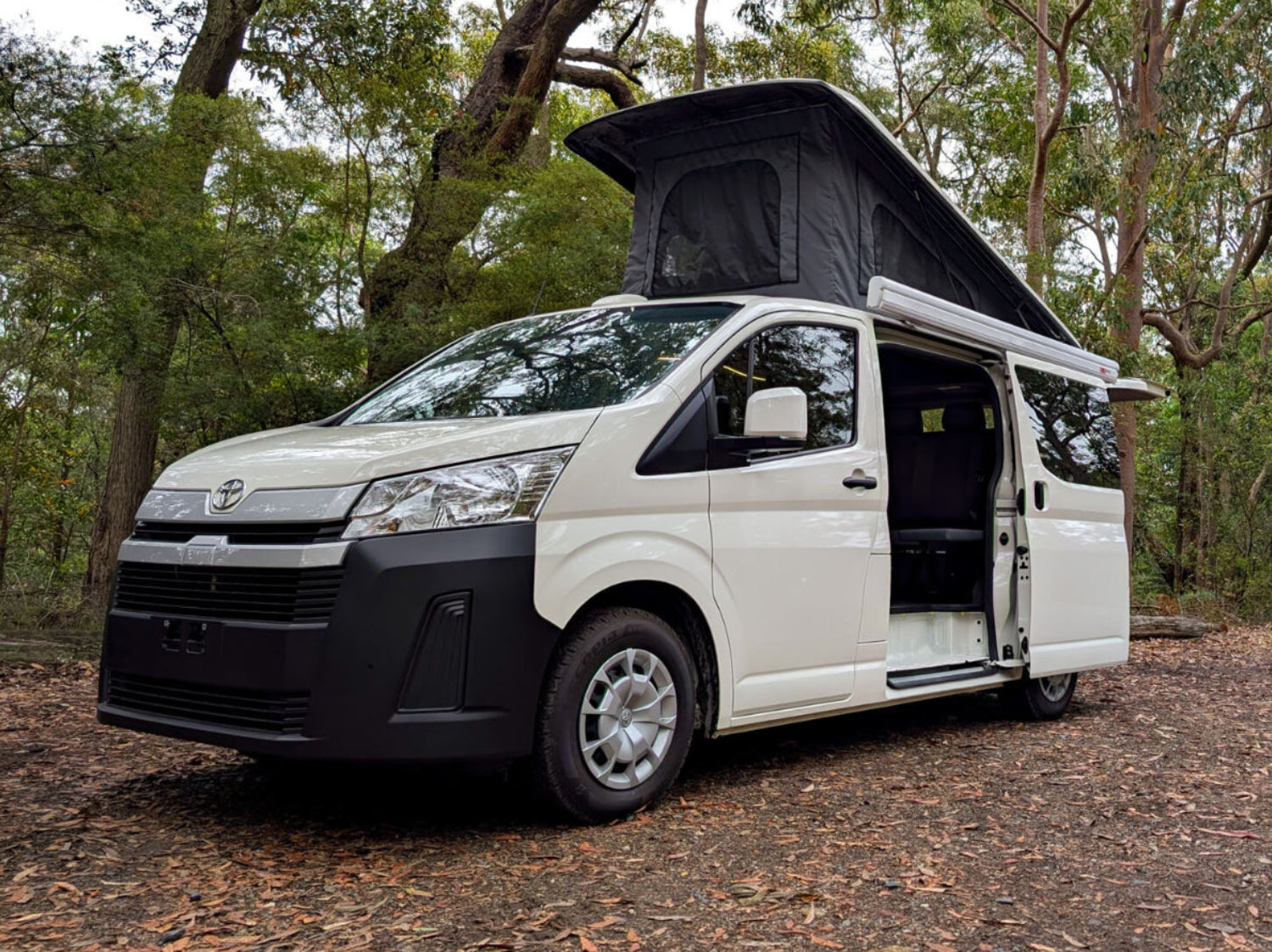 White camper van with open roof in a forest setting