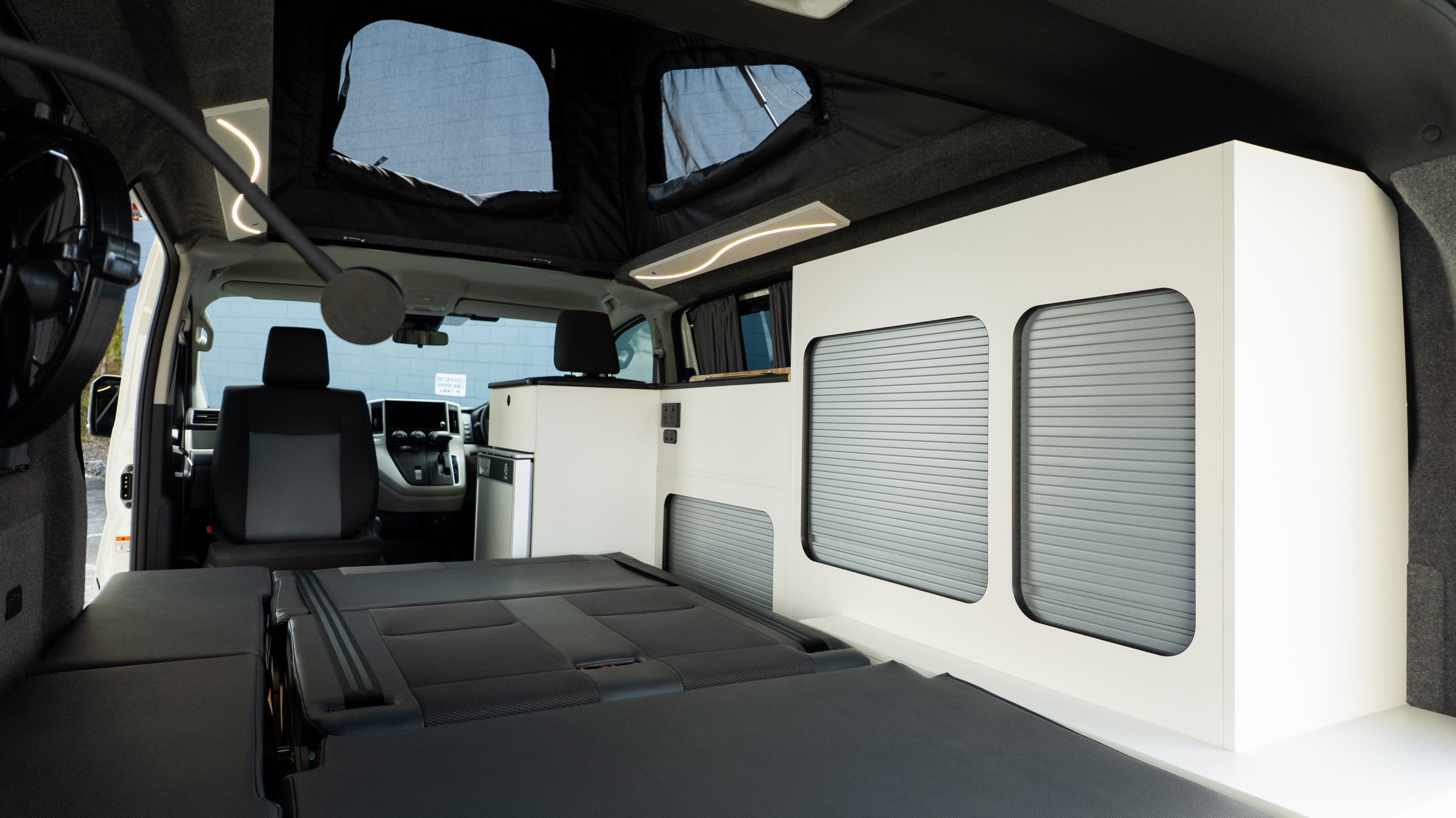 Full Toyota hiace campervan interior shot showing bed folded flat, captain's chair, storage and pop top erected