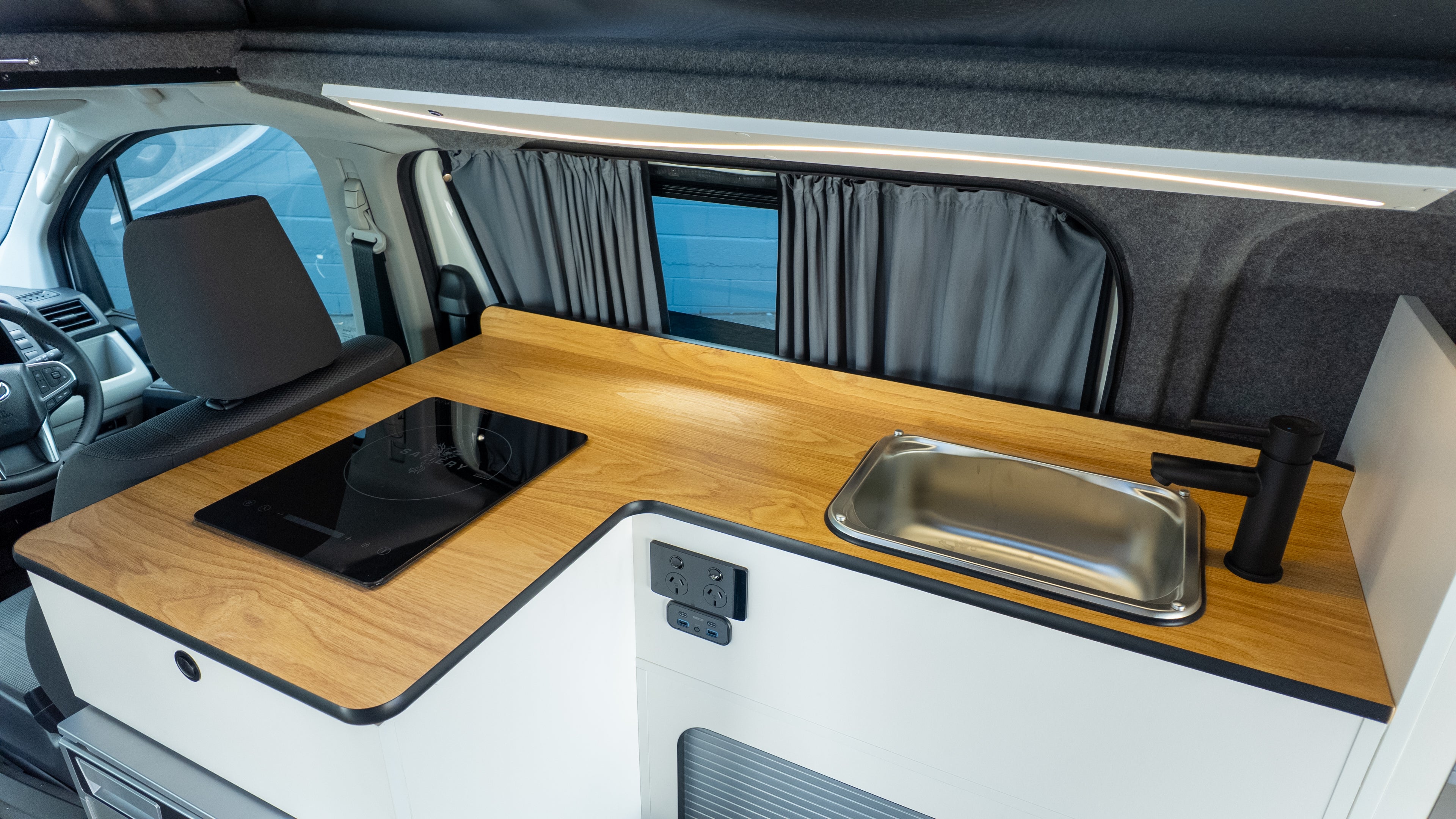 Campervan interior on engineered toyota hiace campervan. Shows internal kitchen, sink, fridge and induction cook top